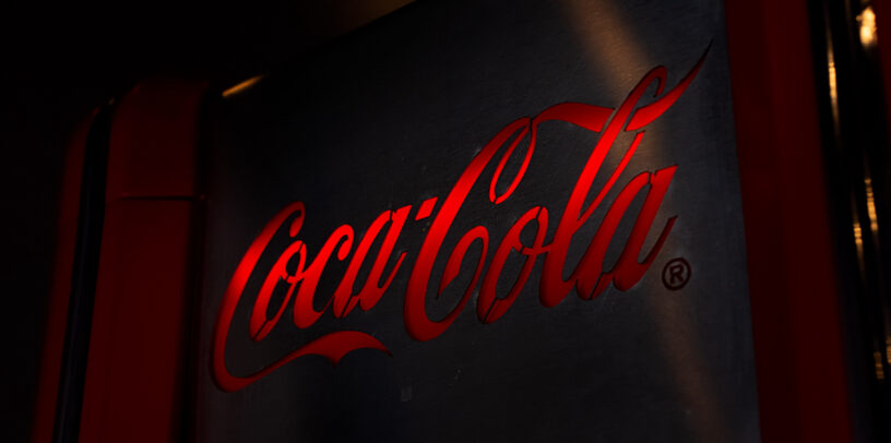 A view of a glowing Coca-Cola vending machine sign in red and in the dark.